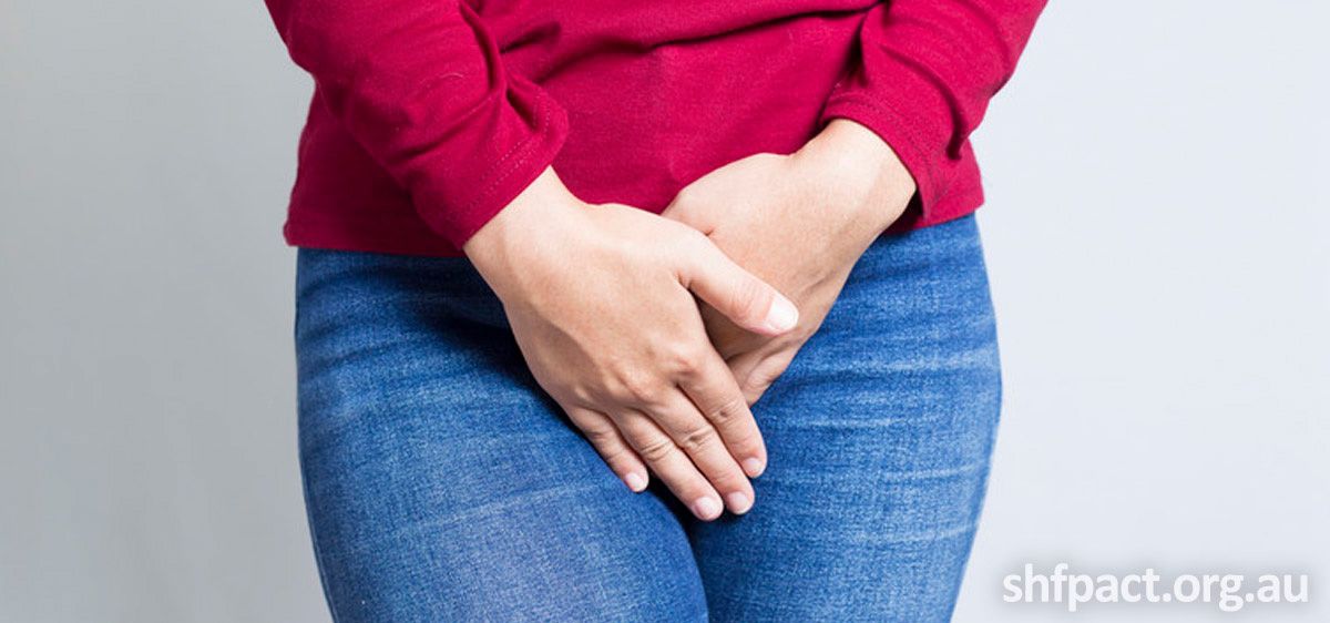 An image of the lower half of a woman with a red top and blue jeans. Her hands are placed over there private area.