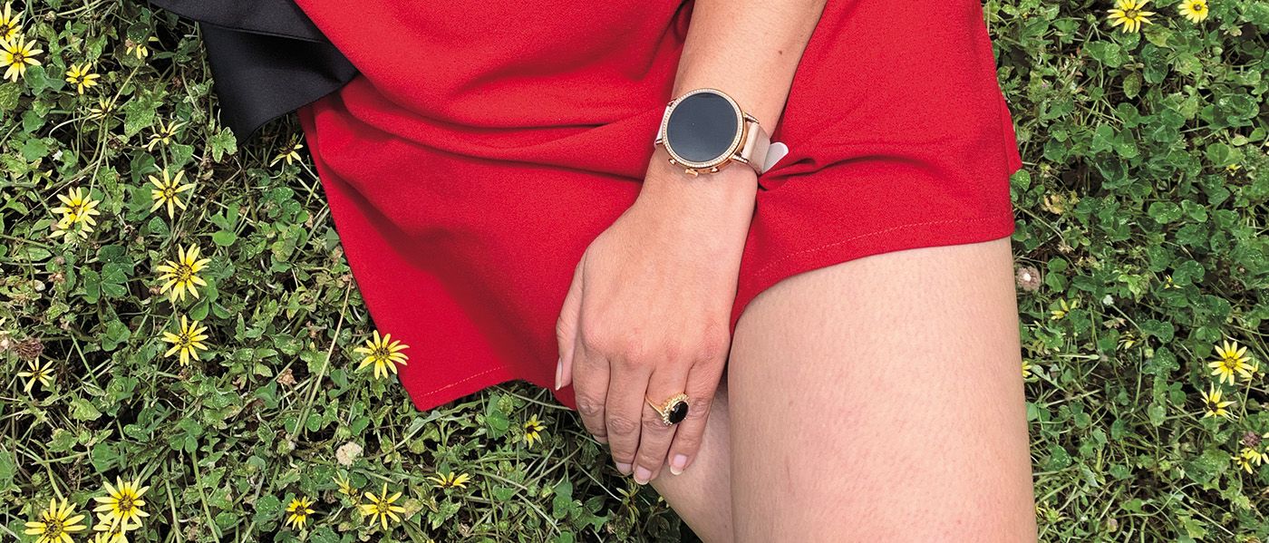 A photo of a woman a red dress sitting on the grass, crossing her legs over.