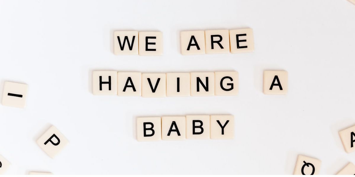 A Photo of scrabble pieces on a white background that say 'We are having a baby'.